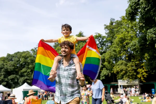 Pai e filho segurando bandeira LGBT em uma passeata de Orgulho LGBTQIAPN+
